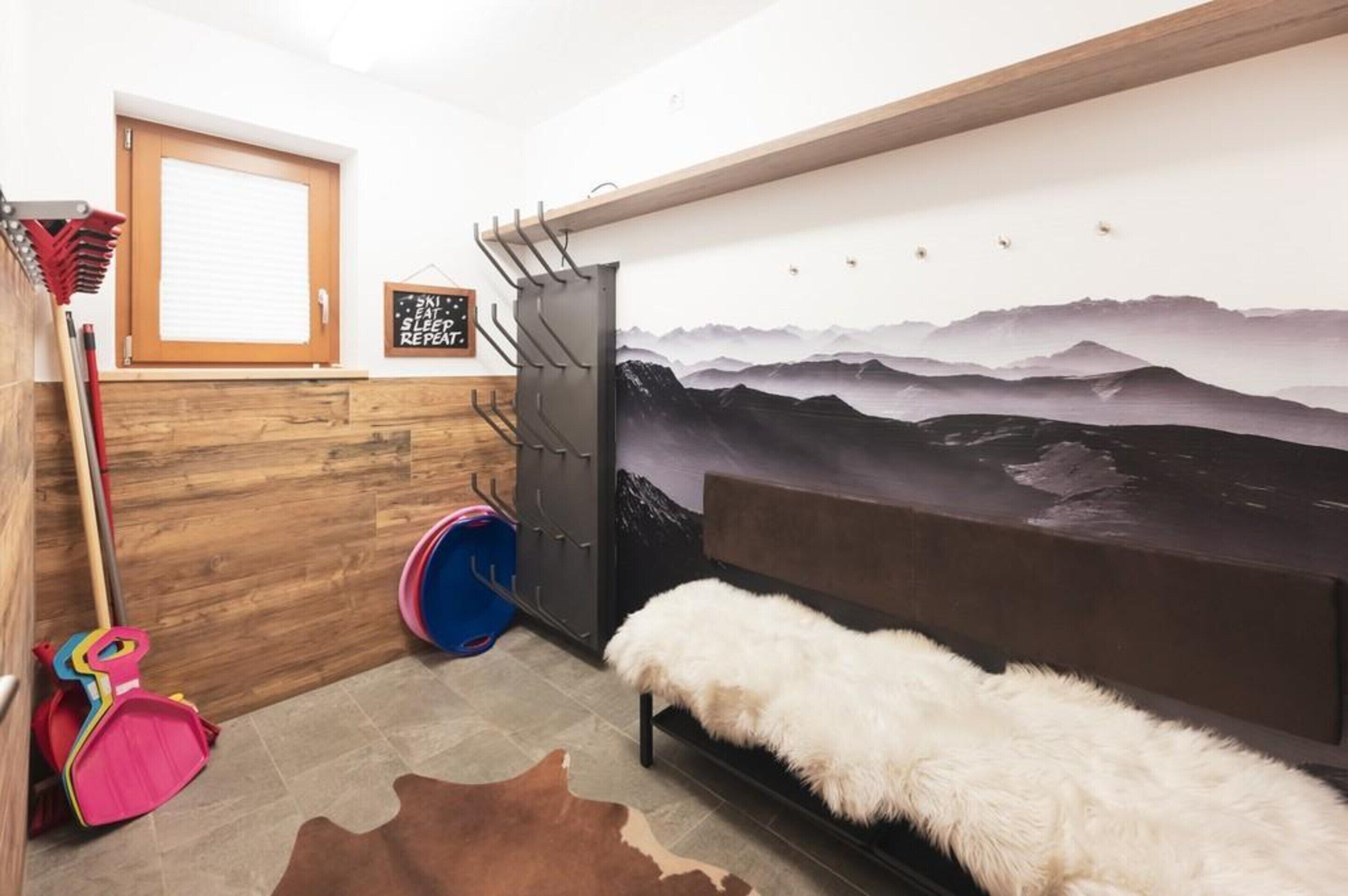 Une pièce avec un lit, un mur en bois, une fresque représentant une montagne, une porte et un petit tapis.