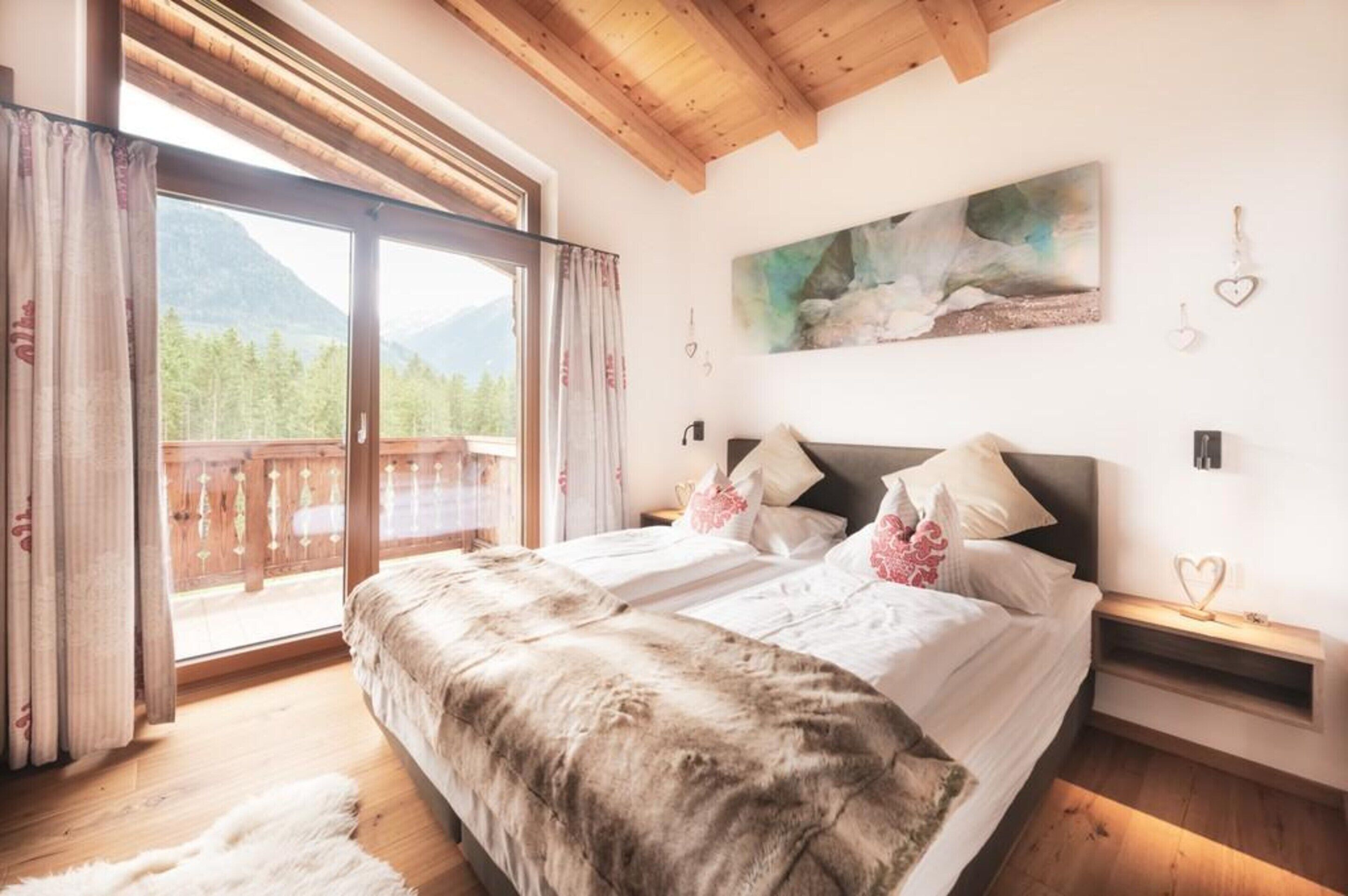 A bedroom with a large bed, wooden headboard, and a view of a mountain landscape through a sliding door.