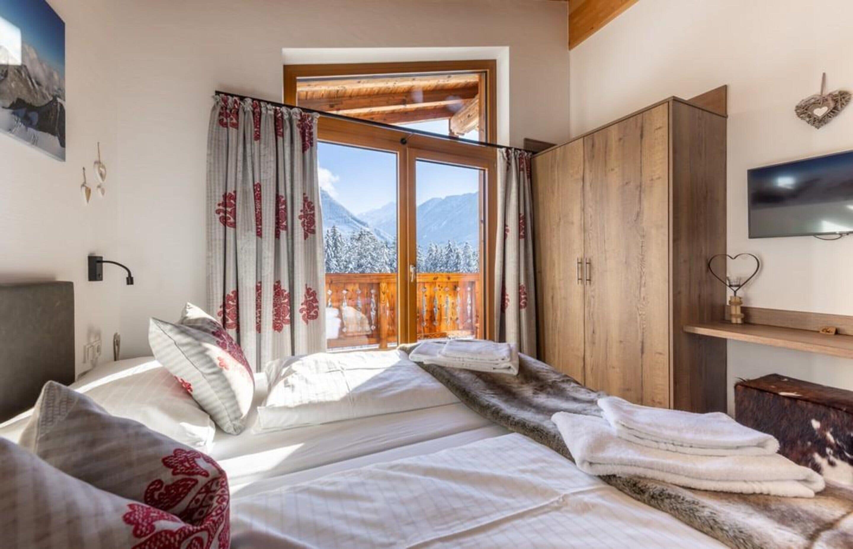 A bedroom with a bed, a wardrobe, a television, and a window with curtains.