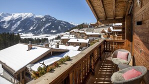 A wooden balcony with a view of snow-covered mountains, wicker chairs, and a wooden railing. - Splendid Chalet in Neukirchen near Wildkogel Ski Arena (Neukirchen am Grossvenediger)