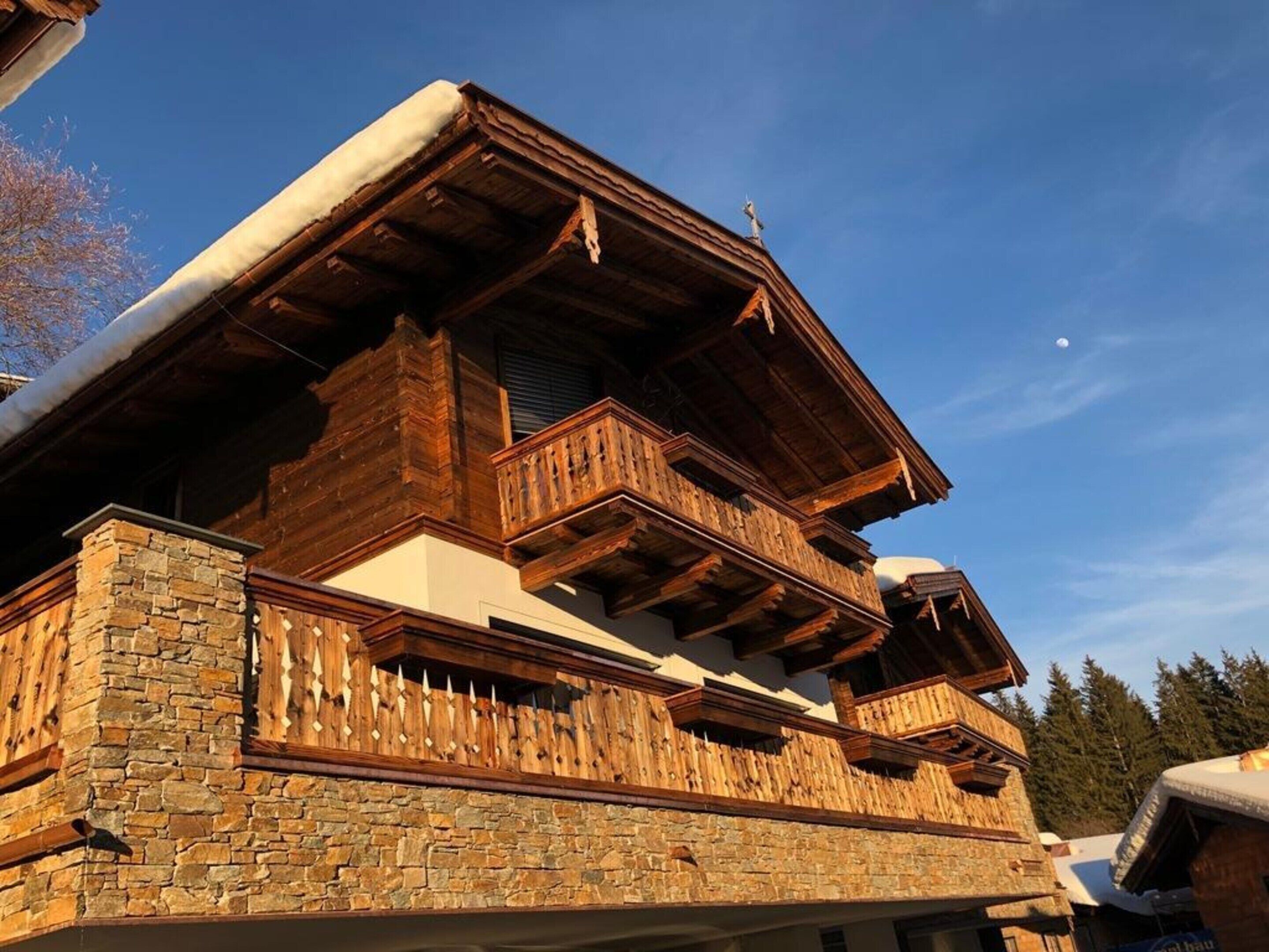 A traditional chalet with a stone facade, wooden balconies, and a clear sky.