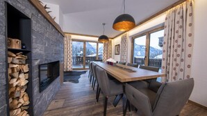 A modern dining area with a stone fireplace, wooden dining table, and grey chairs. - Splendid Chalet in Neukirchen near Wildkogel Ski Arena (Neukirchen am Grossvenediger)