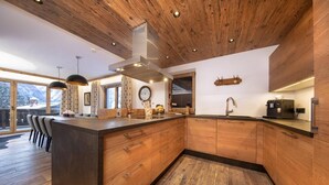 A modern kitchen with wooden cabinetry, a central island, and a large window offering a view of the outdoors. - Splendid Chalet in Neukirchen near Wildkogel Ski Arena (Neukirchen am Grossvenediger)