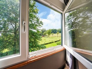 Una ventana con vistas a un paisaje verde, que incluye árboles y un campo.