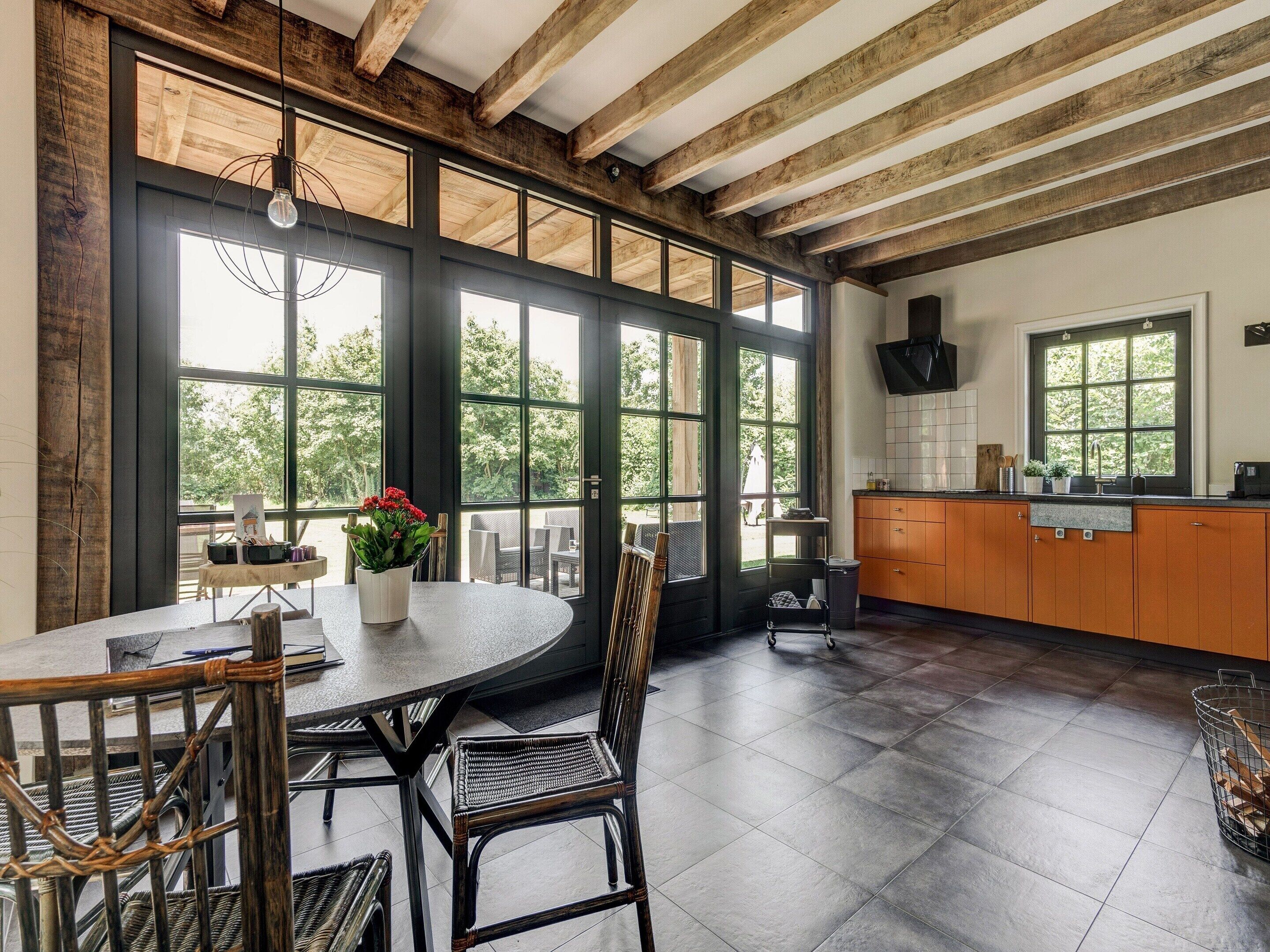 A spacious kitchen with large windows, wooden beams, and a round dining table with wicker chairs.