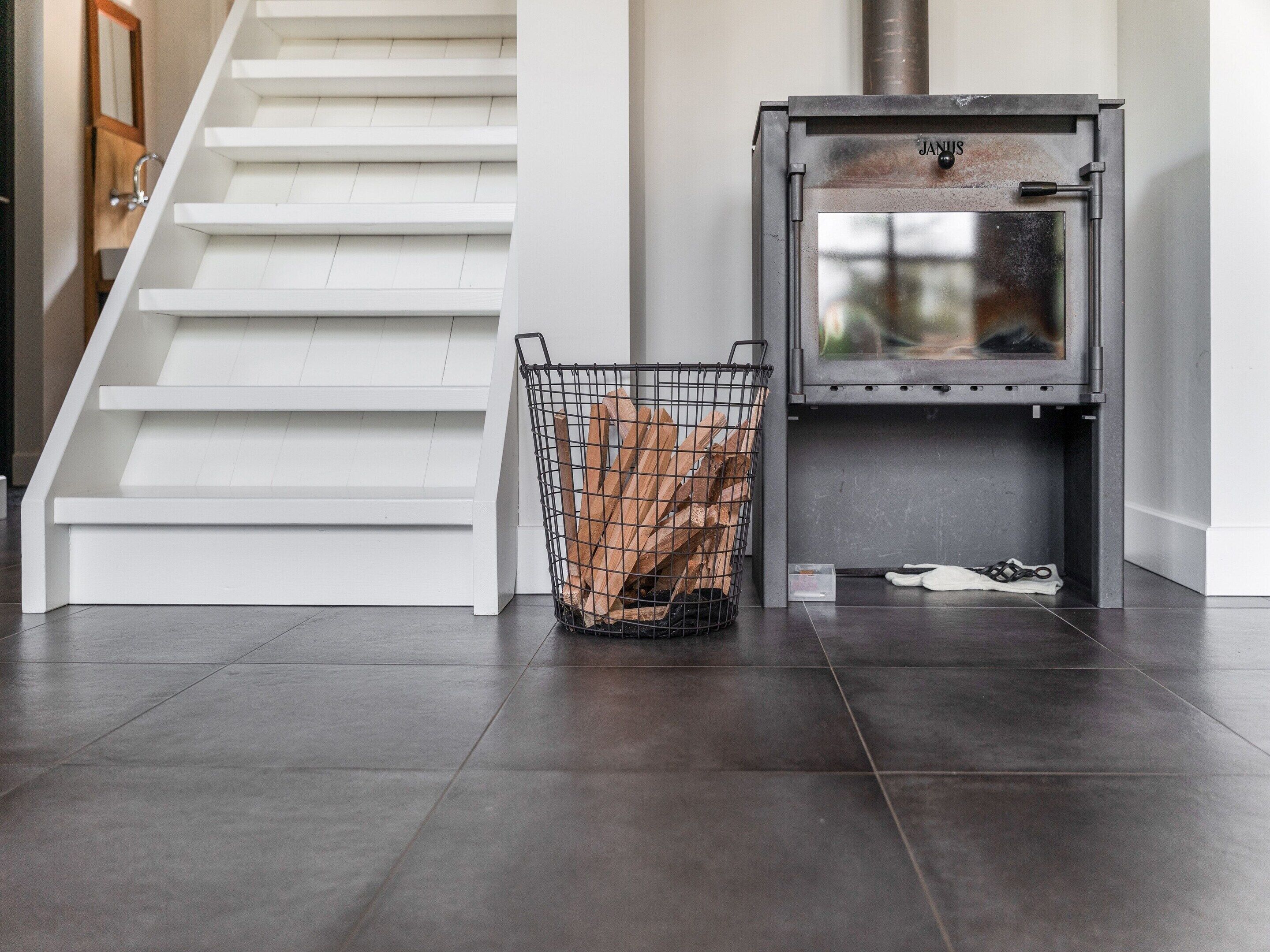 A modern interior with a staircase, a metal basket with logs, and a wood-burning stove.