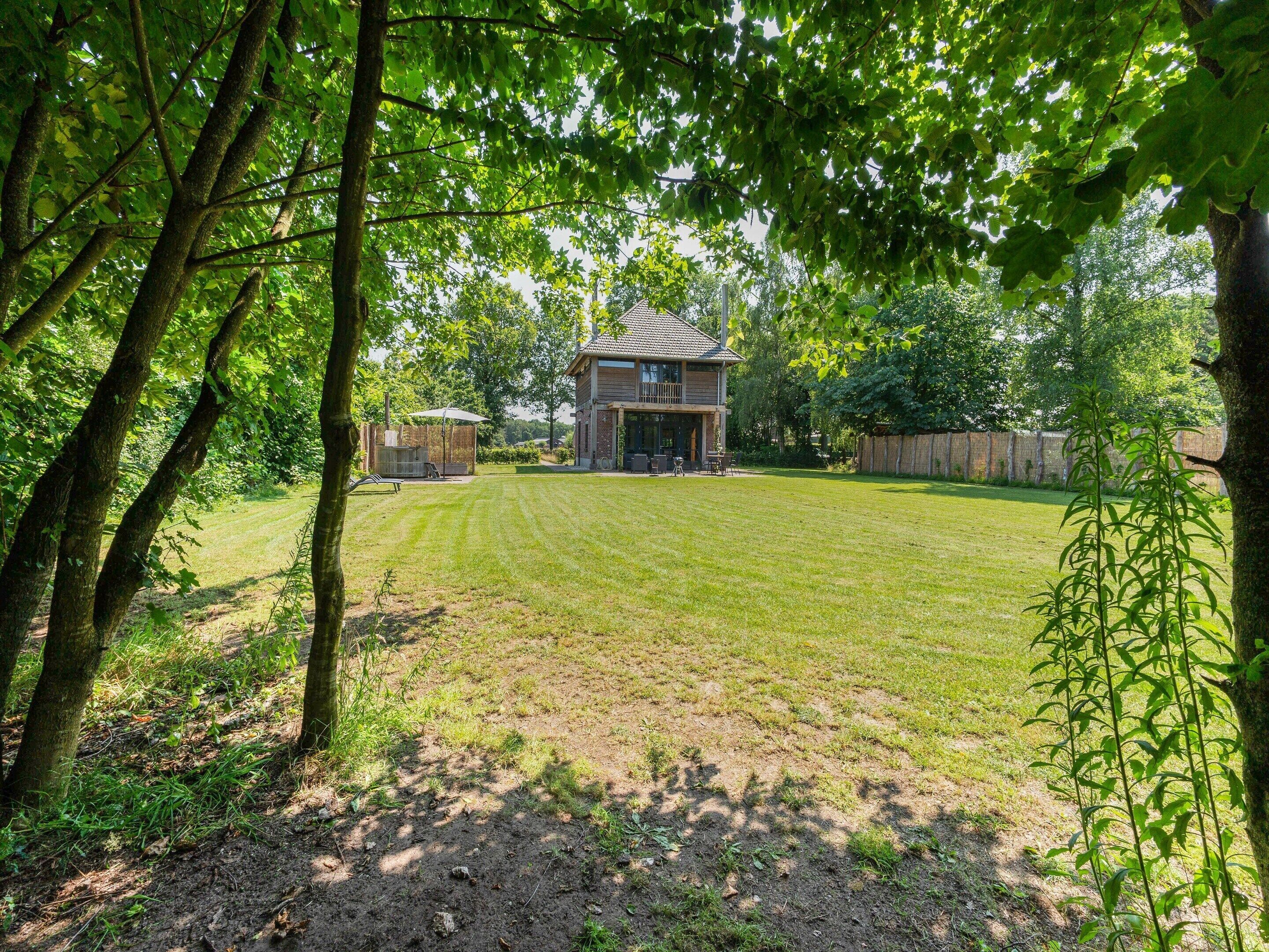 A two-story house with a well-maintained lawn, surrounded by trees and a wooden fence.