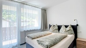 A bedroom with a bed, two bedside tables, a nightstand, and a window with curtains. - Chalet in Kaprun Near Ski Slopes (Kaprun)