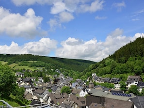 A town with traditional architecture, surrounded by lush green hills and a clear sky.