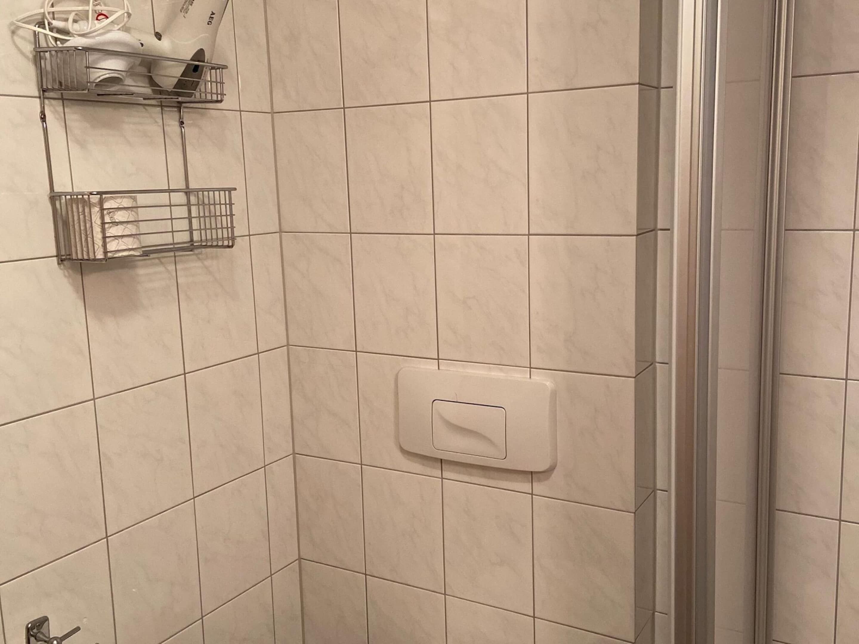A bathroom with white tiles, a shower area, and a hand dryer mounted on the wall.