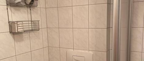 A bathroom with white tiles, a shower area, and a hand dryer mounted on the wall.
