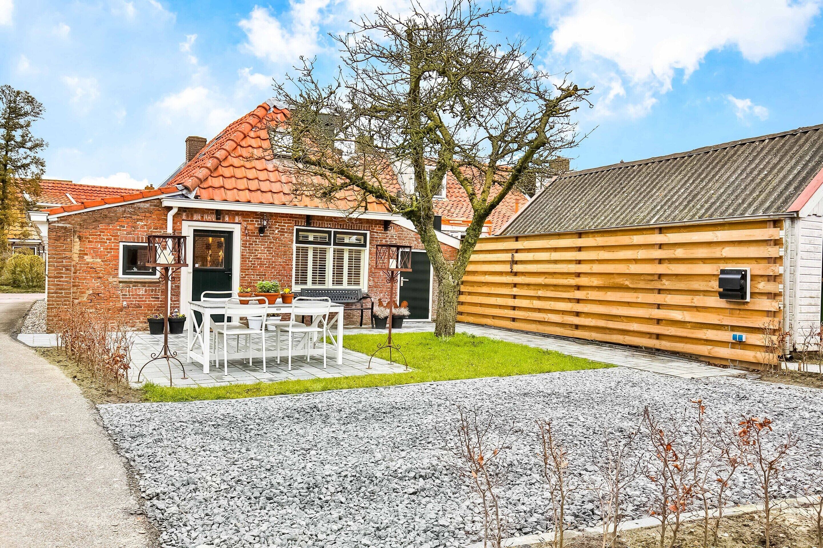 A brick house with a tiled roof, a wooden fence, a gravel driveway, and a small lawn.