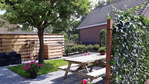 En træterrasse med et picnicbord, omgivet af krukker med planter og et træhegn.