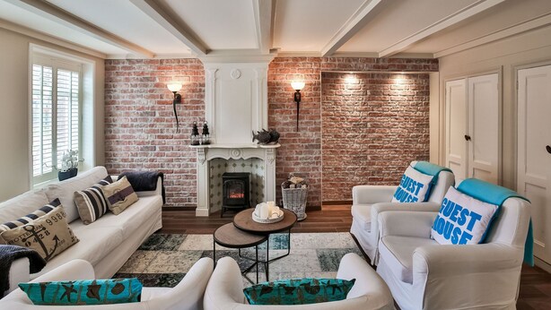 A cozy living room with a brick wall, white furniture, a fireplace, and a "Guest House" sign.
