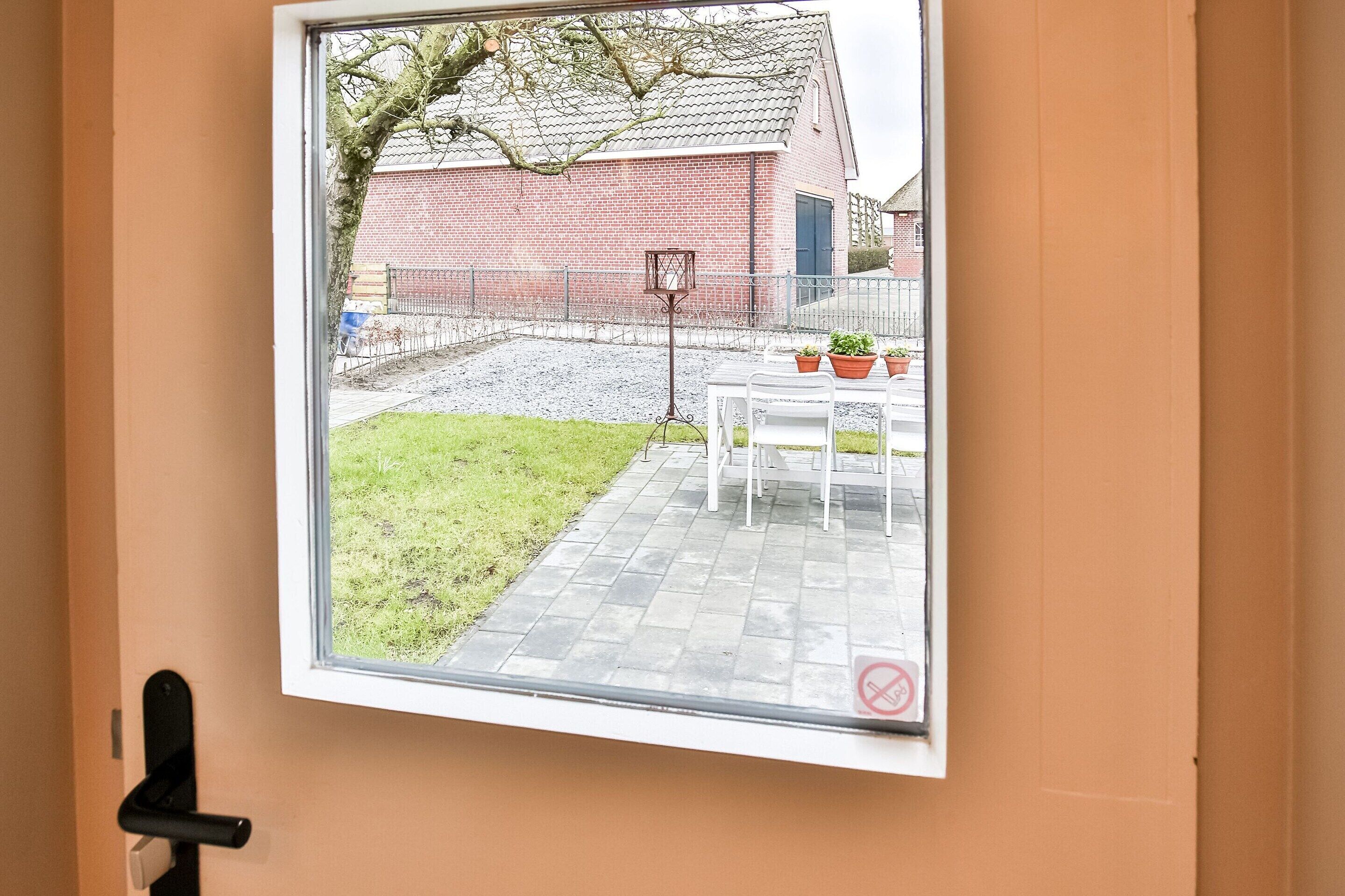 A window with a view of a brick building, a grassy area, and a table with potted plants.