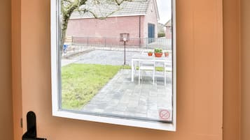 A window with a view of a brick building, a grassy area, and a table with potted plants.