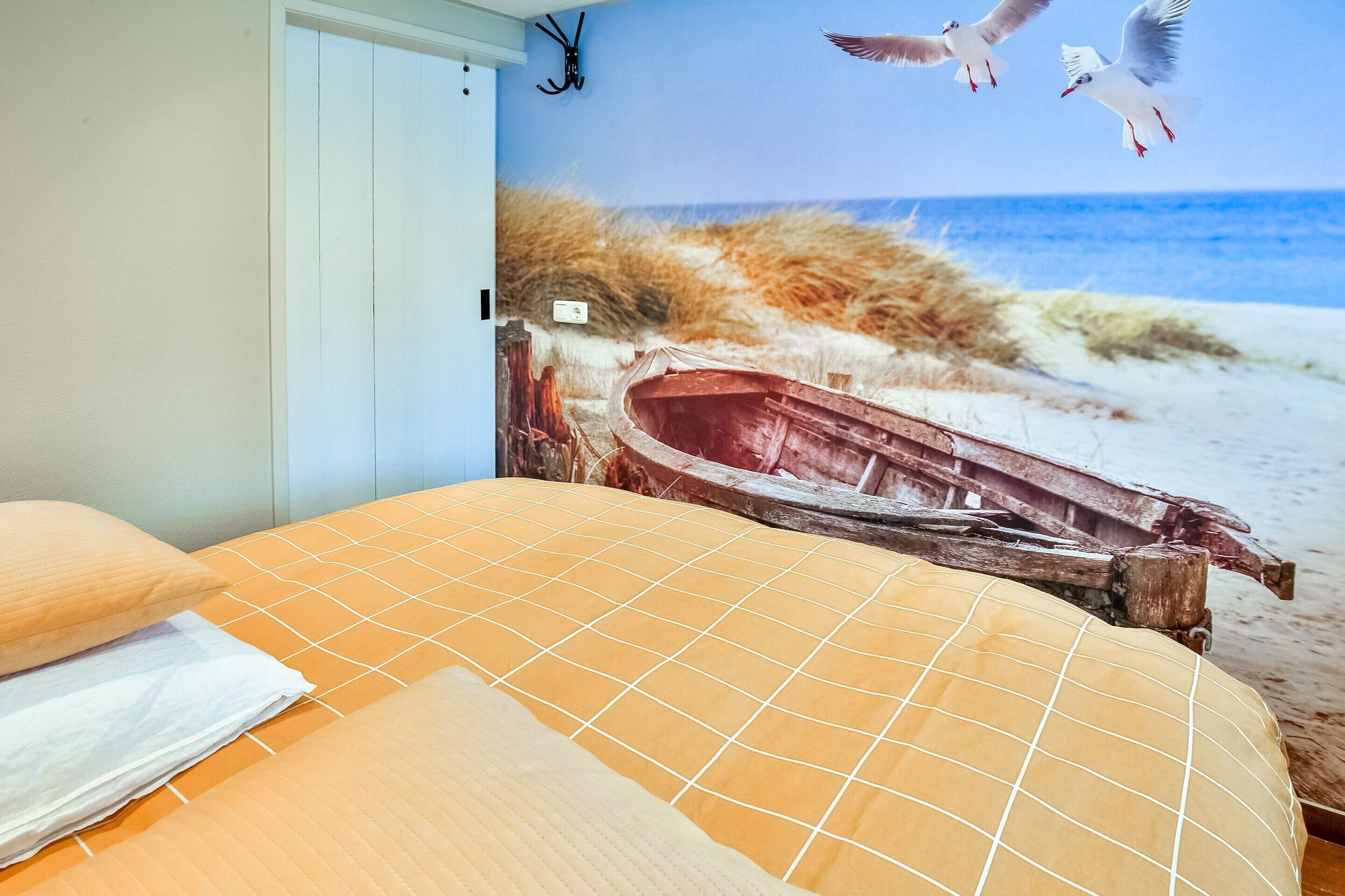A bedroom with a large mural of a beach scene, including a boat and seagulls.