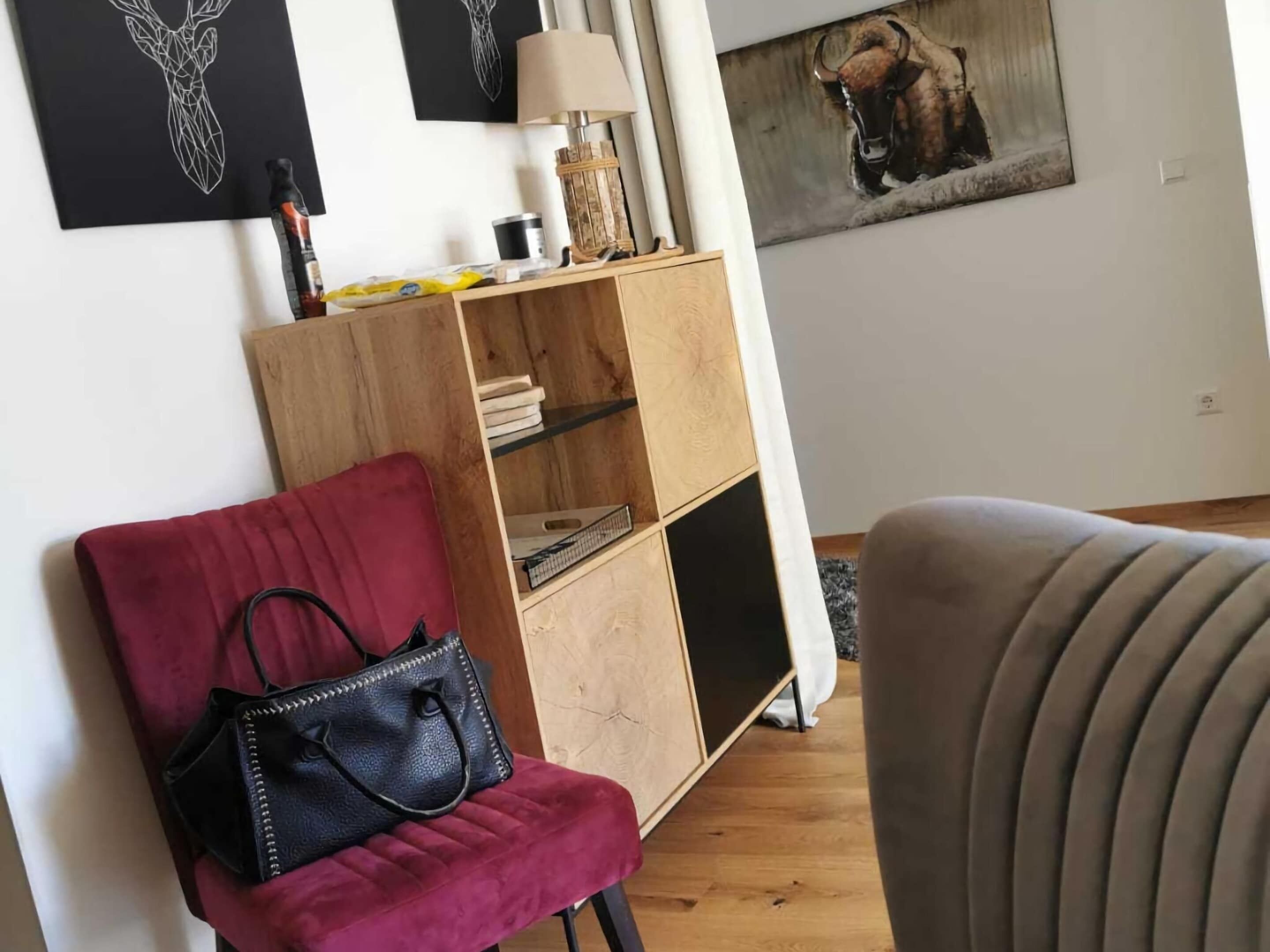 A living room with a red chair, a black handbag, a wooden bookshelf, and a painting of a bison.