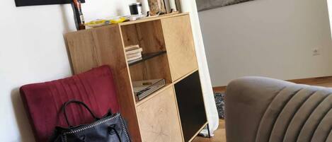 A living room with a red chair, a black handbag, a wooden bookshelf, and a painting of a bison.
