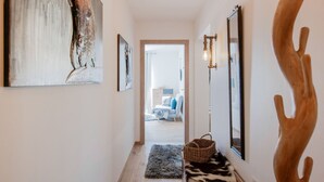 A hallway with a wooden floor, a rug, a woven basket, a wooden bench, and two wall-mounted light fixtures.