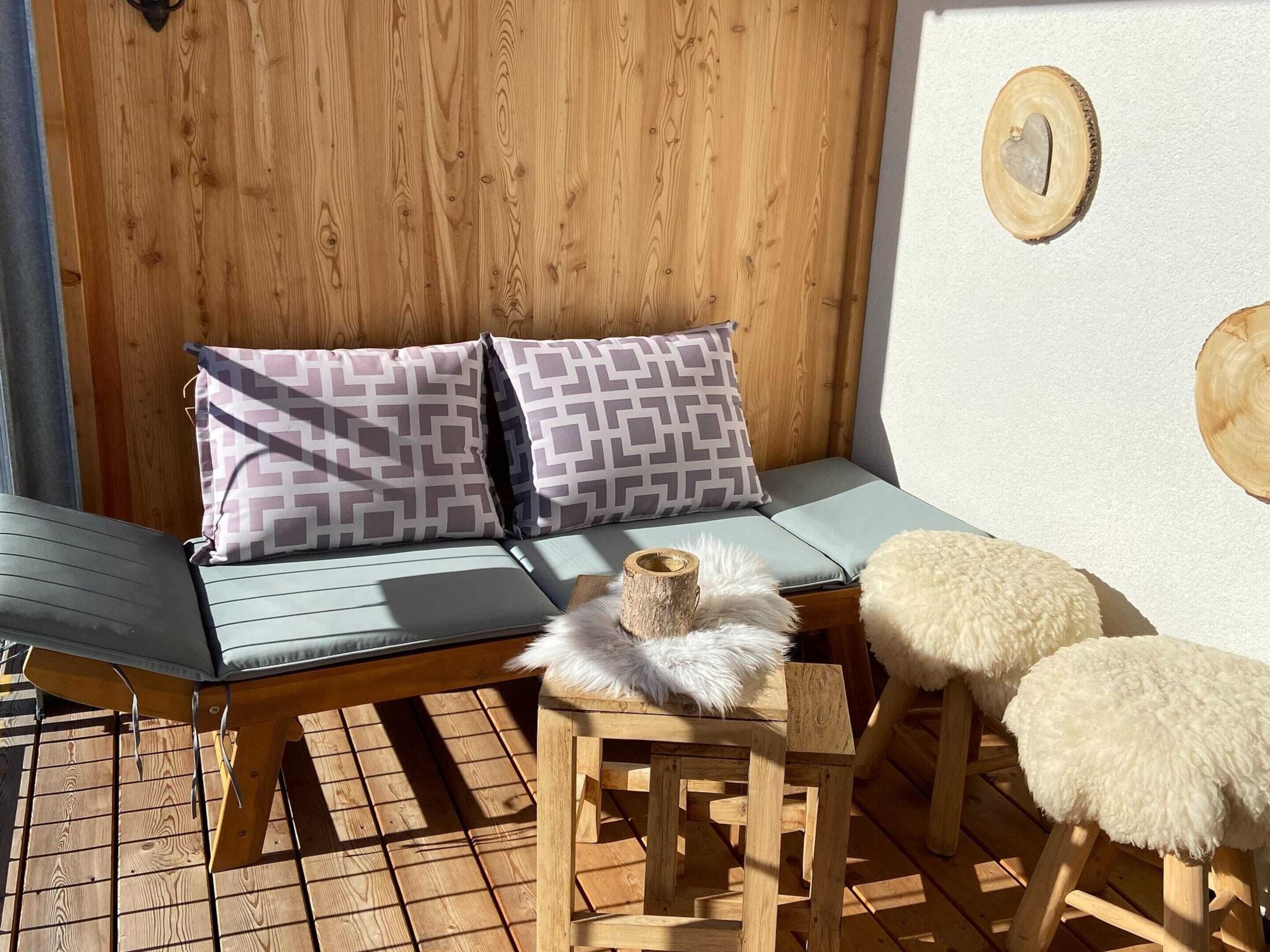 A wooden deck with a cushioned seating area, a small table, and a decorative wooden piece on the wall.