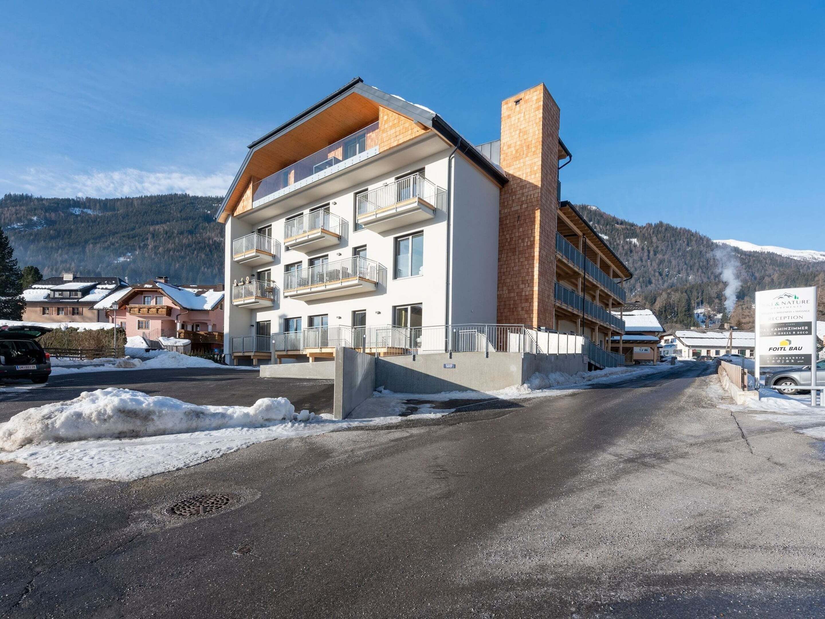 Ein mehrstöckiges Hotel mit Balkonen, einem Ziegelkamin und einem Parkplatz mit Schnee.