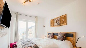 A bedroom with a large bed, a mounted TV, a window with curtains, and a wooden headboard.