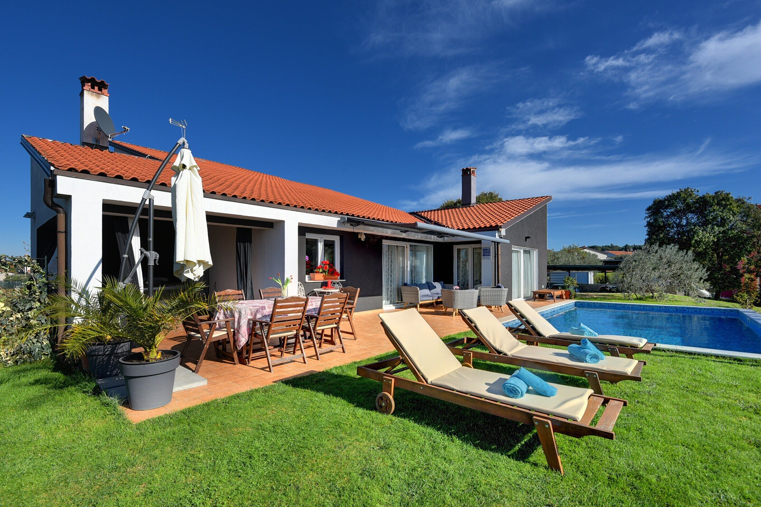 A house with a swimming pool, outdoor seating, and a well-maintained lawn.