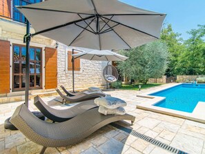 A poolside area with wicker lounge chairs, a hanging chair, and a stone sculpture. - Villa in a Typical Istrian Rustical Style (Sveti Lovrec)
