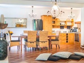 A modern kitchen with wooden cabinets, a stainless steel refrigerator, and a dining area with wicker chairs and a chandelier. - Villa in a Typical Istrian Rustical Style (Sveti Lovrec)