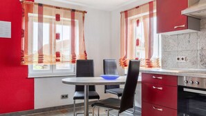 Eine kleine Küche mit einem runden Tisch, zwei schwarzen Stühlen, roten Schränken und einem eingebauten Backofen.