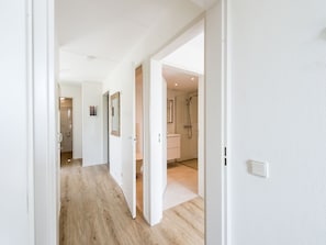 Ein moderner Flur mit Holzboden, weißen Wänden und Türen zu einem Badezimmer sowie einer Dusche.
