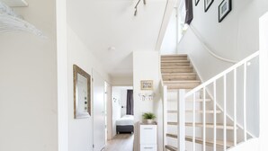 Ein Flur mit Treppe, Holzboden, weißen Wänden und einem kleinen Nachttisch mit Pflanze.