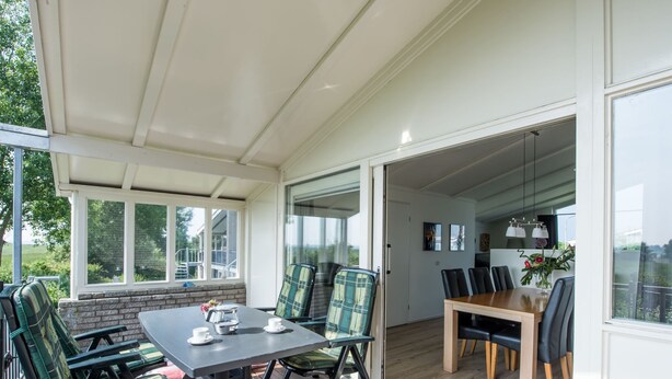 Ein überdachter Patio-Bereich mit Tisch und Stühlen, ein Holzboden und Blick ins Freie.