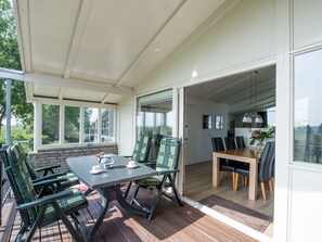 Un patio cubierto con mesa y sillas, piso de madera y vistas al exterior.