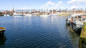 A calm river with boats docked on the right, a church spire in the background, and residential buildings along the riverbank. - Holiday Home in Medemblik With Garden (Medemblik)