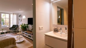 A modern hotel room with a large window, a flat-screen TV, a comfortable chair, a small round table, and a neatly organized bookshelf. - Holiday Home in Medemblik With Garden (Medemblik)