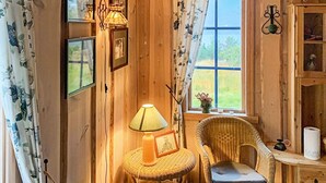 A cozy room with wooden walls, a wicker chair, a small table with a lamp, and a window with a view of greenery. - 6 Person Holiday Home in Ostereidet (Alver)
