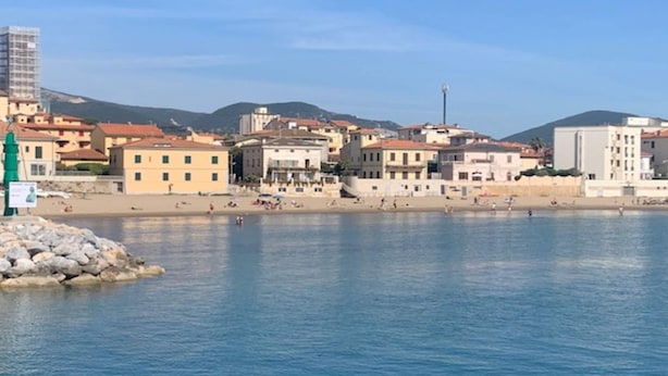 A coastal town with buildings along the waterfront, a clear sky, and a rocky outcrop with a sign. - Holiday Gome in San Vincenzo Near Beach (San Vincenzo)