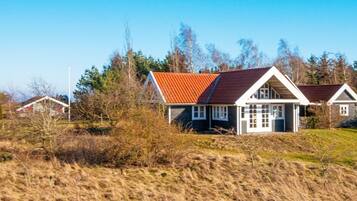 A house with a red roof and white walls, surrounded by trees and a grassy field.