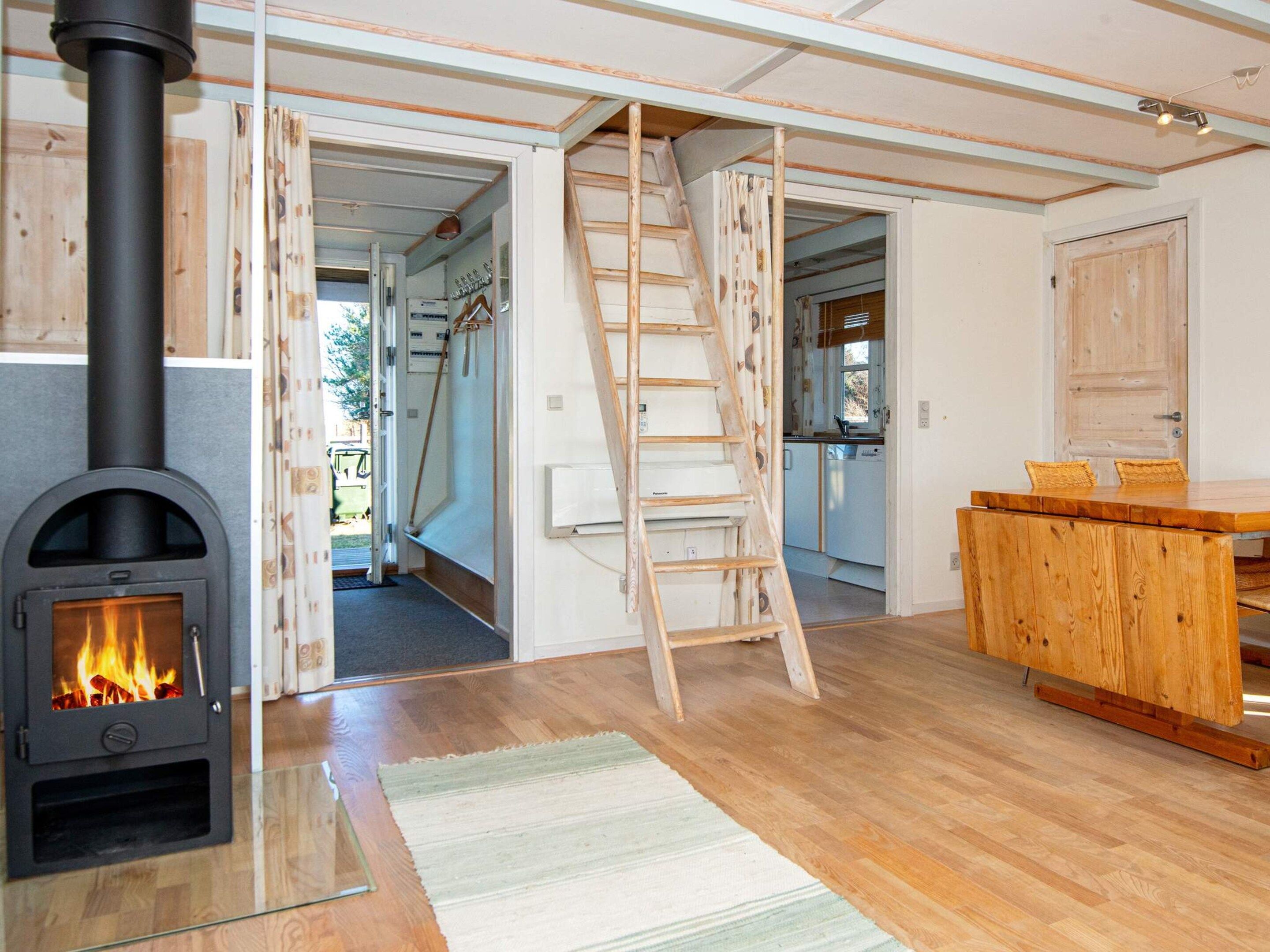A room with a wood-burning stove, a wooden ladder, a kitchen area, and a wooden dining table.