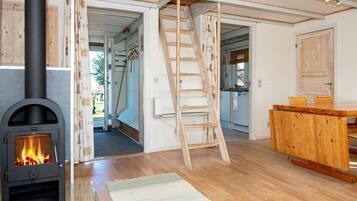 A room with a wood-burning stove, a wooden ladder, a kitchen area, and a wooden dining table.