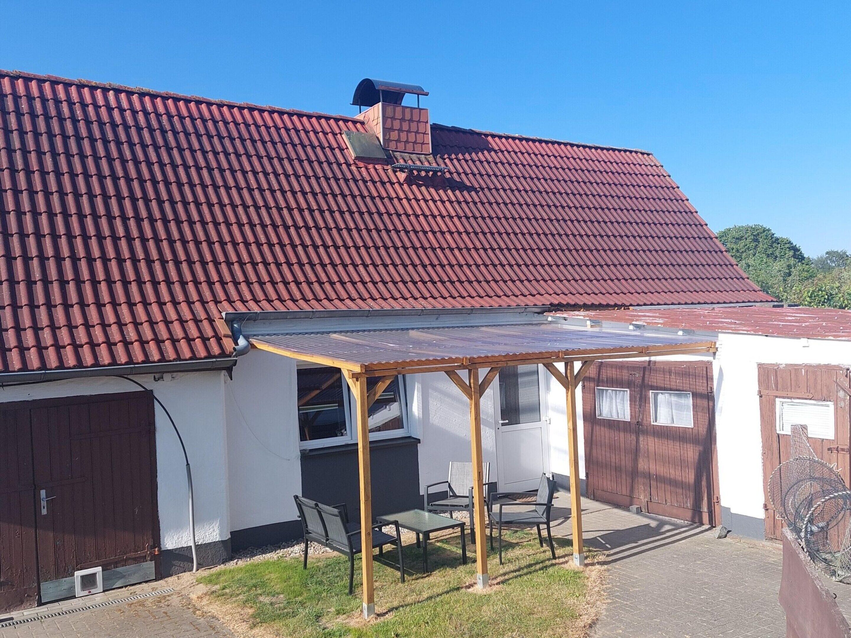 Un espace extérieur aménagé, abrité et doté d’une table et de chaises, d’une pergola en bois et d’un toit recouvert de tuiles rouges.