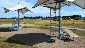 Un parque infantil con estructuras para escalar, columpios y zonas con sombra.