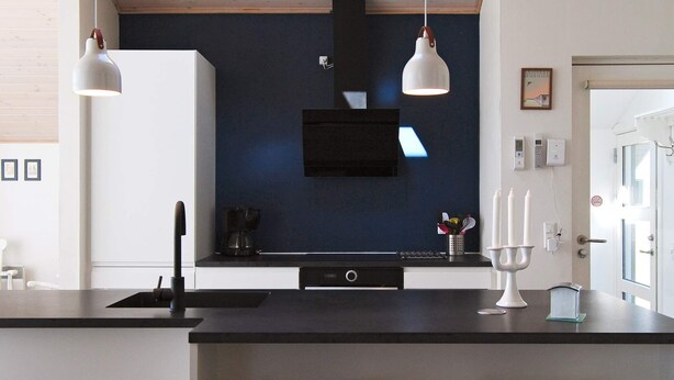 Una cocina moderna con una encimera negra, dos taburetes de madera, una cafetera y luces colgantes.