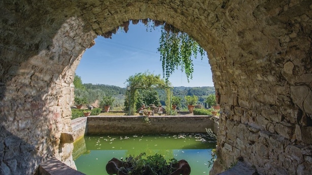 A stone archway with a view of a green pond and trees in the background. - Tuscany Bliss: Garden Retreat (San Casciano in Val di Pesa)