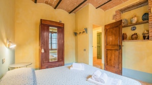 Un dormitorio con cama, una puerta de madera, una mesita y un estante con adornos.