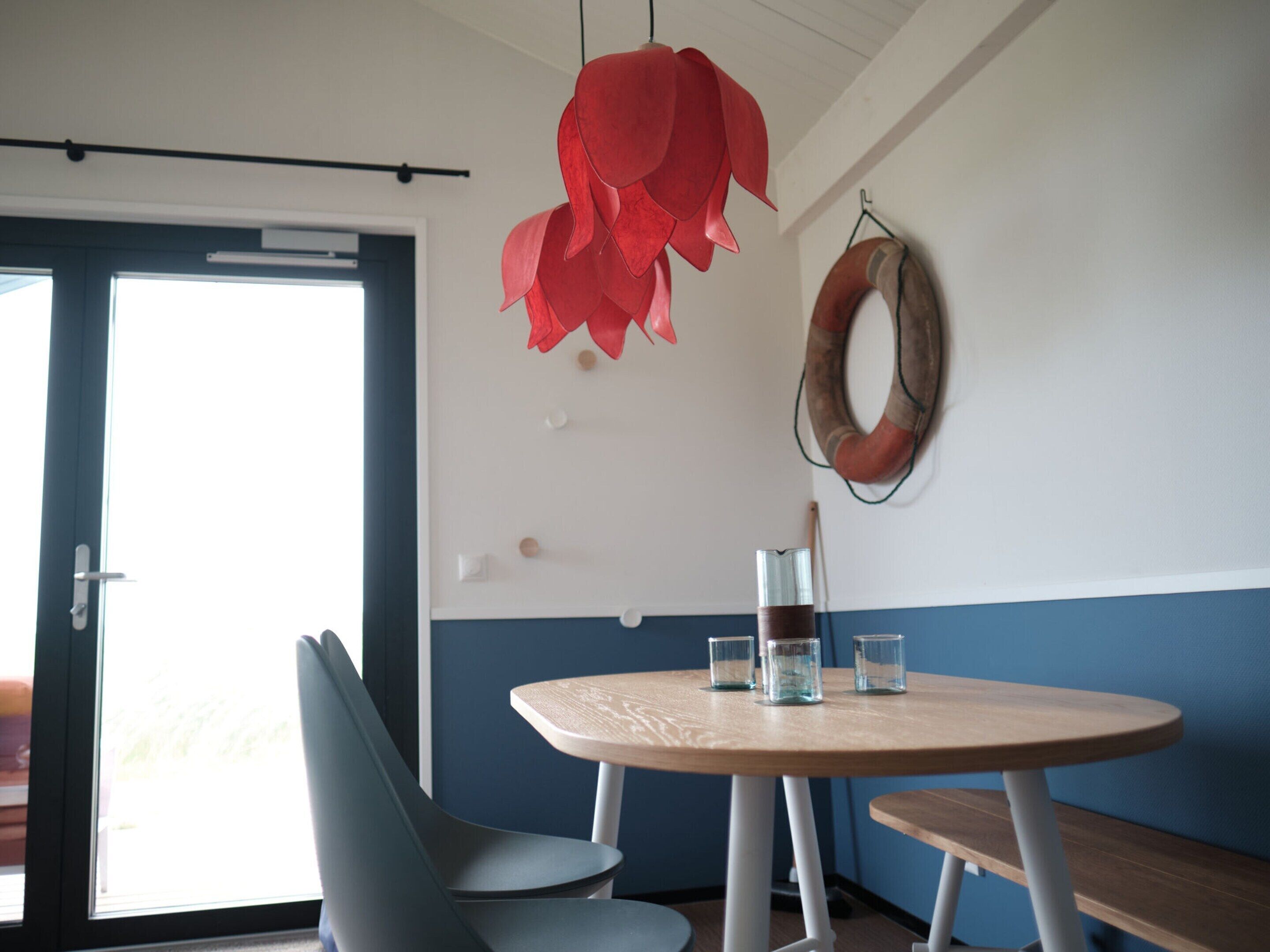 Une pièce avec une table ronde, deux chaises, une décoration florale rouge suspendue et une couronne en bois accrochée au mur.