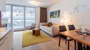A modern living room with a sofa, coffee table, and dining table. There is a large window with a view of a snowy landscape. - Nice Apartment With Dishwasher, Near the Ski Slopes (Radstadt)