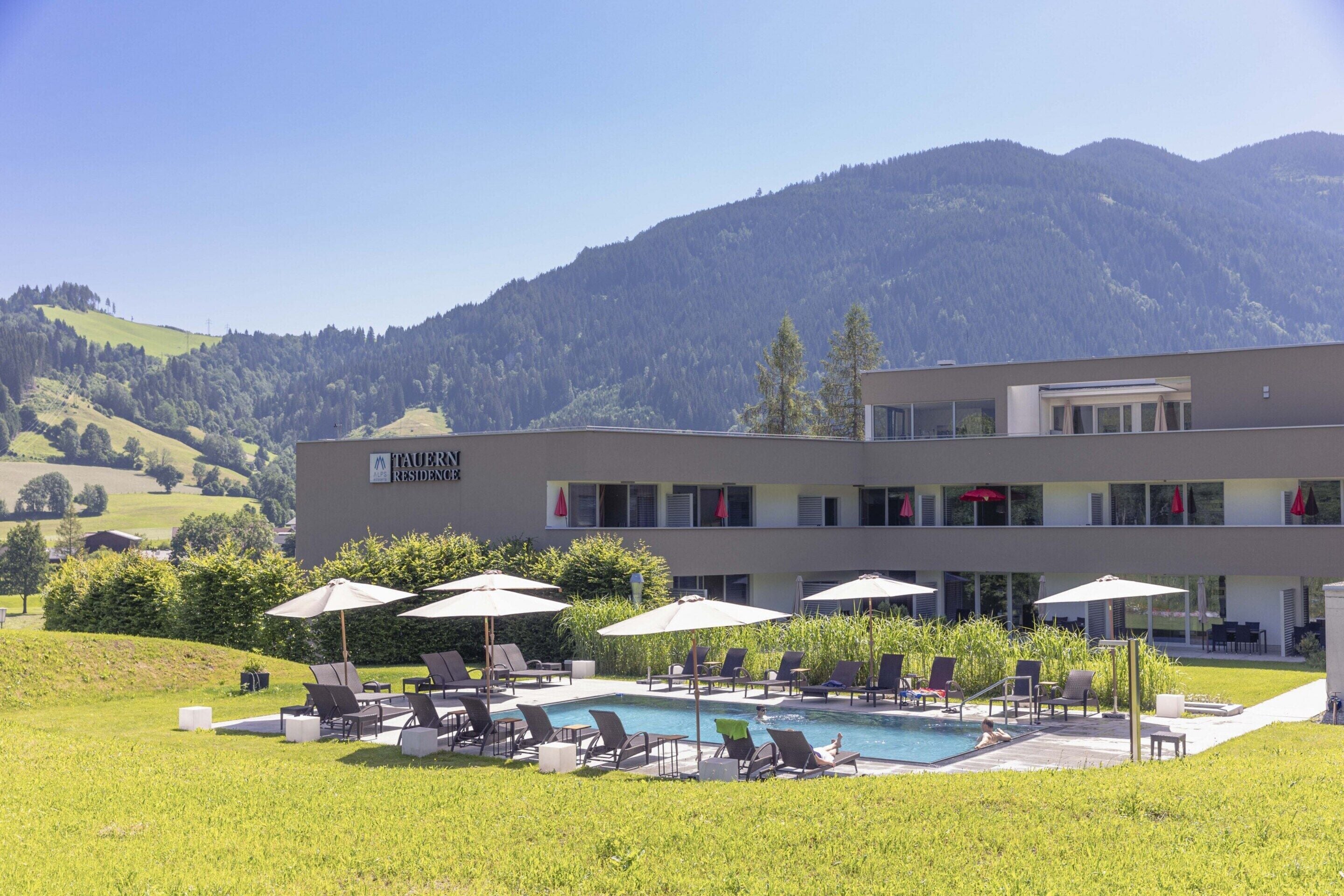 A modern building with a pool area, outdoor seating, and a view of mountains.